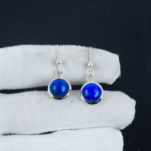 Silver earrings with blue gemstones on a white cloth against a black background