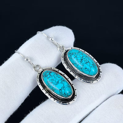 Turquoise earrings with silver frames on a white cloth background