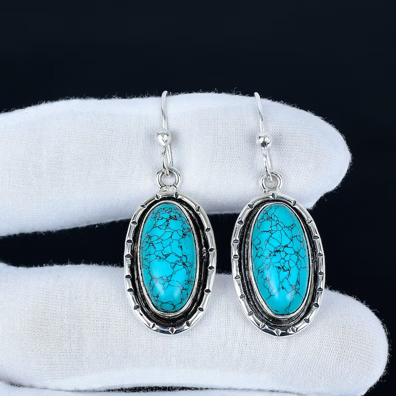Turquoise earrings with silver frames on a white cloth against a black background