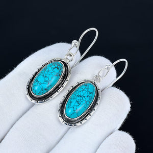 Turquoise earrings with silver frames on a white glove against a black background