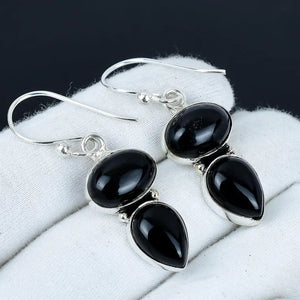 Black teardrop earrings with silver hooks on a white cloth background