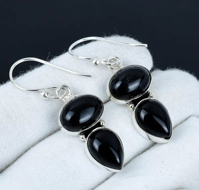 Black teardrop earrings with silver hooks on a white cloth background