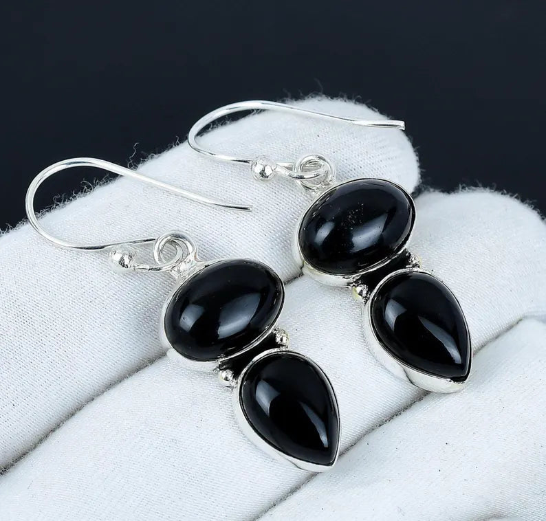 Black teardrop earrings with silver hooks on a white cloth background