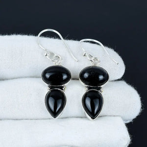 Black teardrop earrings with silver hooks on a white fabric background
