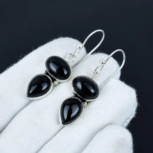 Black teardrop earrings on a white surface with a dark background