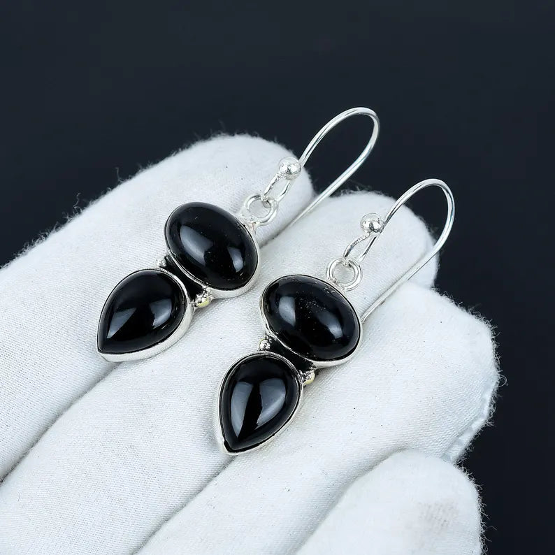 Black teardrop earrings on a white surface with a dark background