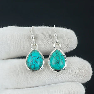 Turquoise teardrop earrings with silver hooks on a white cloth background