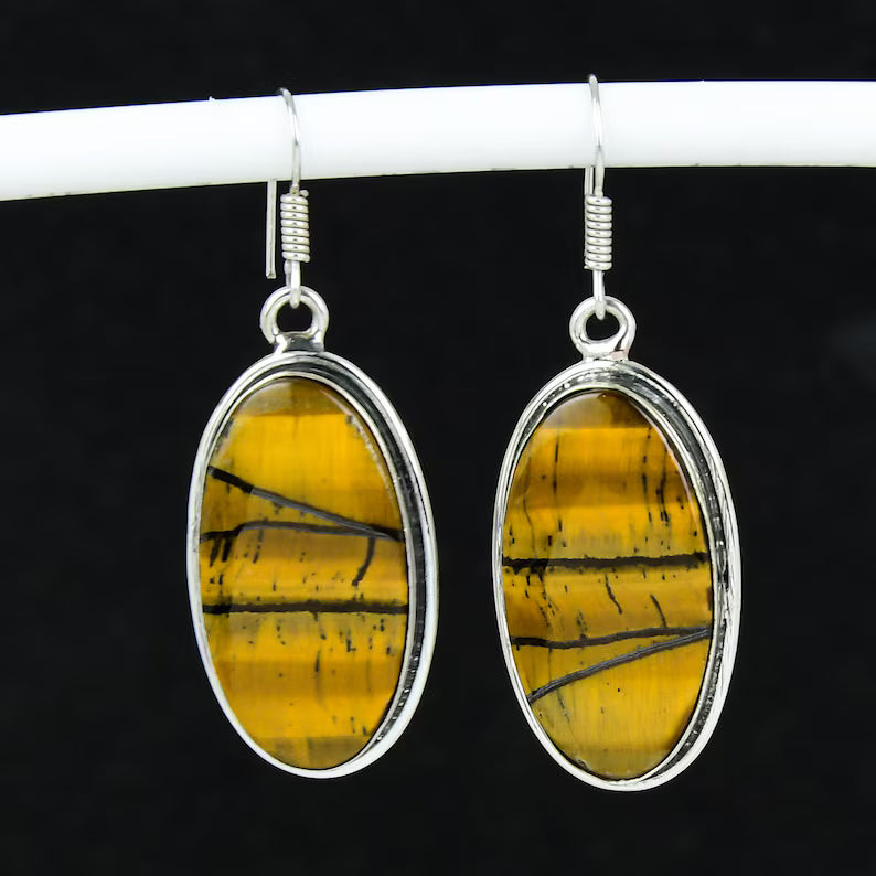 Pair of yellow tiger eye oval earrings with silver frames on a black background