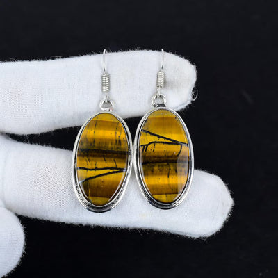 Pair of earrings with yellow gemstones and silver frames on a white cloth.