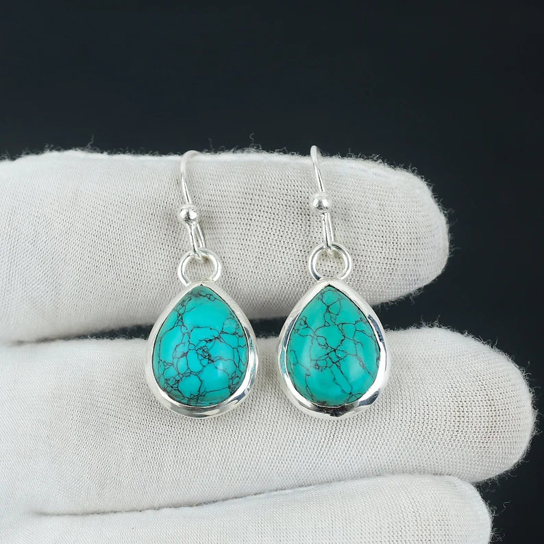 Turquoise teardrop earrings with silver hooks on a white cloth background