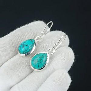 Turquoise teardrop earrings on a white hand with a black background