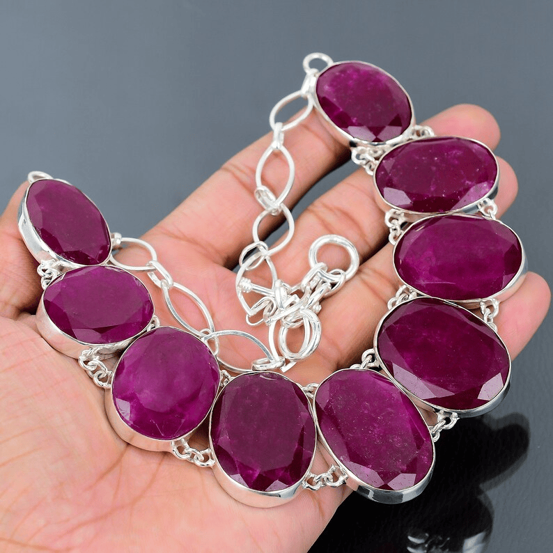 Silver bracelet with purple gemstones held in a hand against a dark background