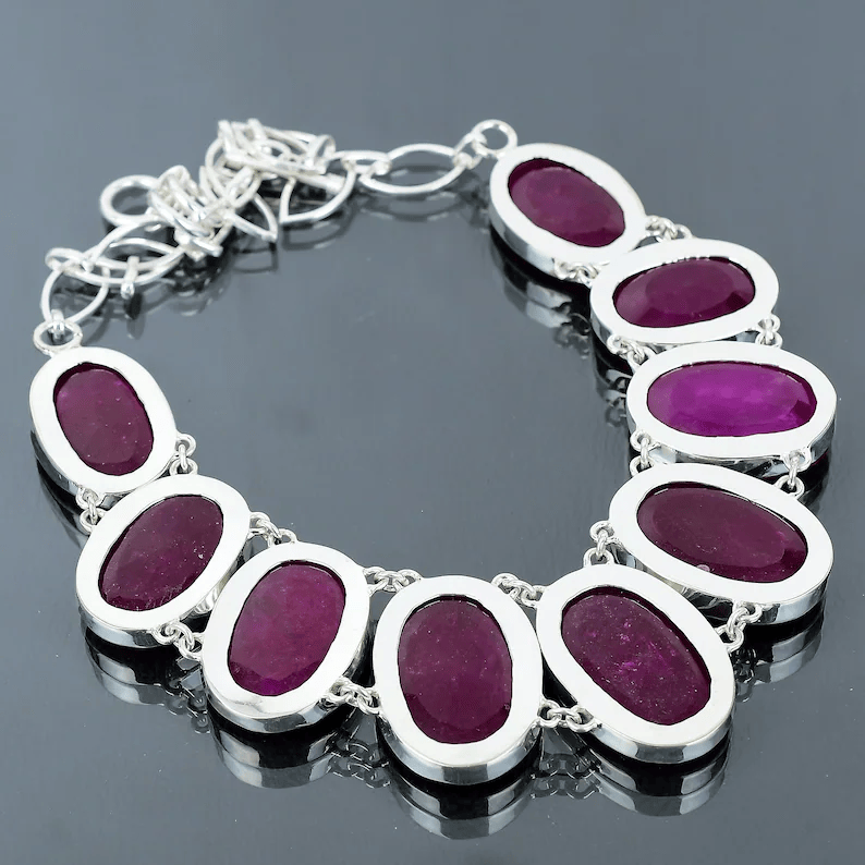Silver bracelet with purple gemstones on a reflective surface