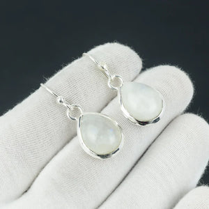 Teardrop-shaped moonstone earrings on a white glove with a black background