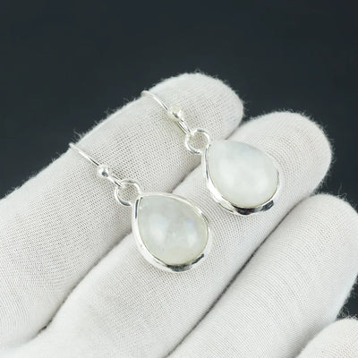 Teardrop-shaped moonstone earrings on a white glove with a black background
