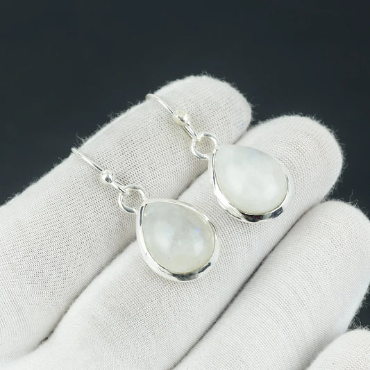 Teardrop-shaped moonstone earrings on a white glove with a black background