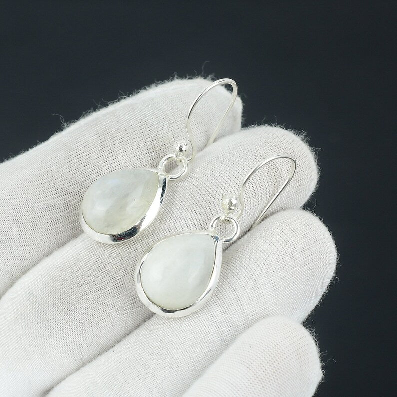 Silver earrings with teardrop-shaped moonstone stones on a white glove against a black background