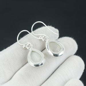 Silver teardrop earrings on a white glove with a dark background