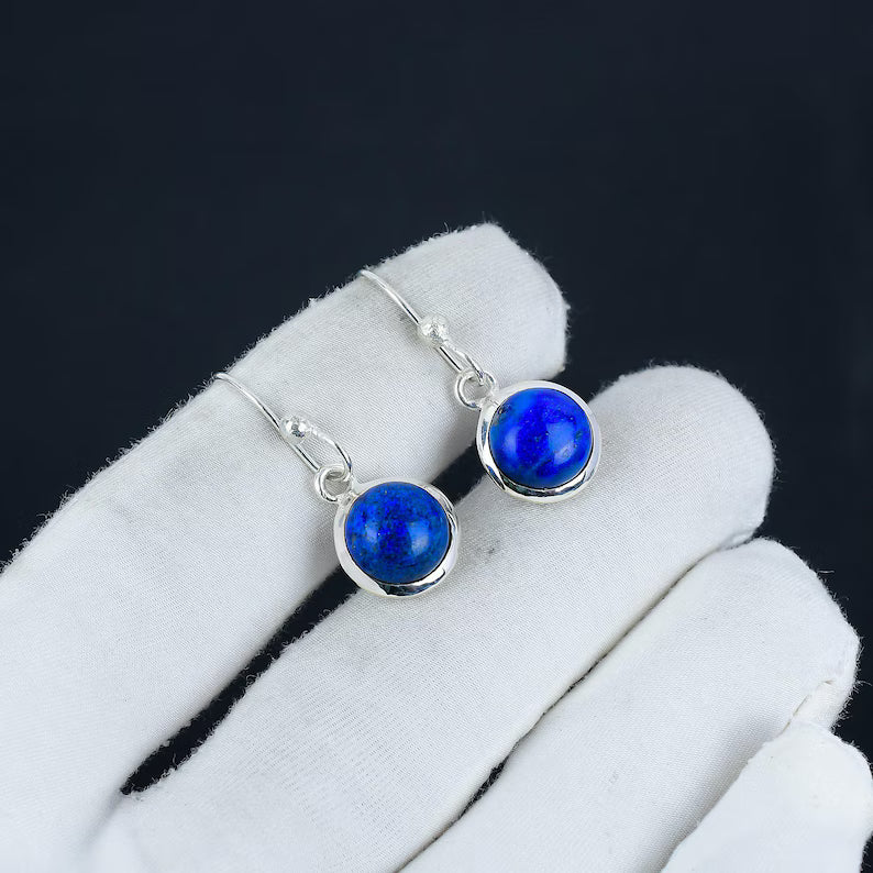 Silver earrings with blue gemstones on a white glove against a black background