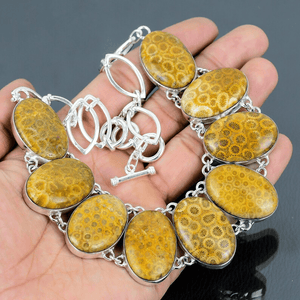 Bracelet with yellow stone and silver chain held in a hand against a dark background