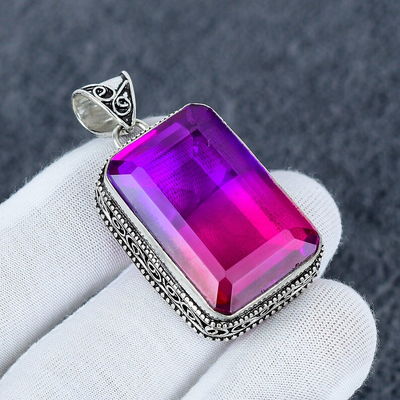 Purple gemstone pendant with silver frame on a white glove against a dark background