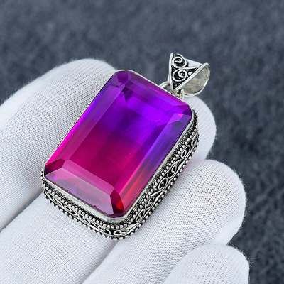 Purple gemstone pendant with silver frame held by a gloved hand against a dark background