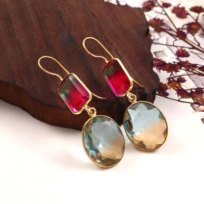 Gold earrings with red and green gemstones on a wooden surface