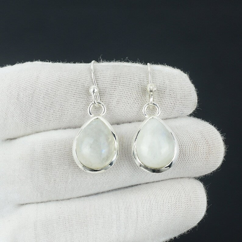Teardrop-shaped silver earrings with light-colored gemstones on a white cloth background