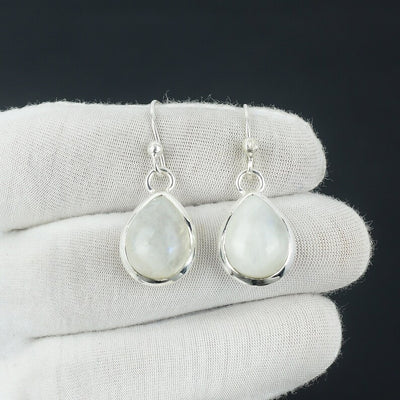 Teardrop-shaped silver earrings with light-colored gemstones on a white cloth background