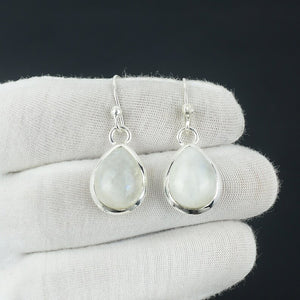 Teardrop-shaped silver earrings with light-colored gemstones on a white cloth background