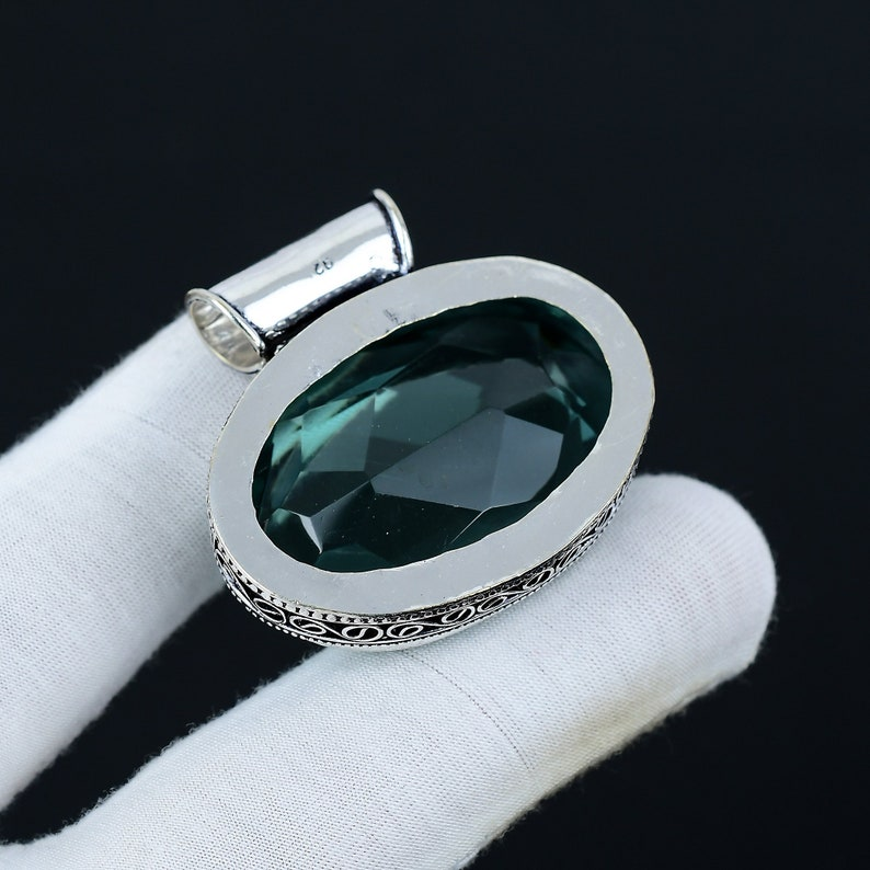 Silver pendant with a green gemstone on a white glove against a black background