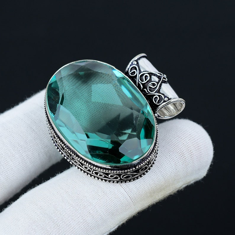 Silver ring with a large green gemstone on a white cloth against a black background