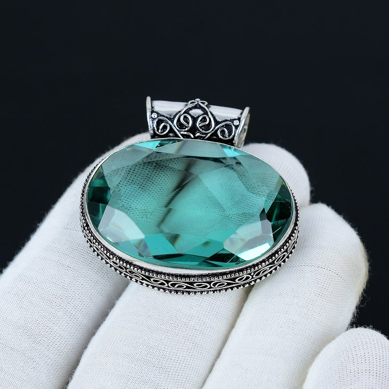 Green gemstone pendant with silver setting held by a gloved hand against a black background