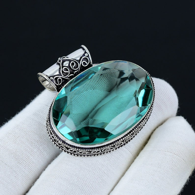 Jewelry pendant with a large green gemstone on a white cushion against a black background