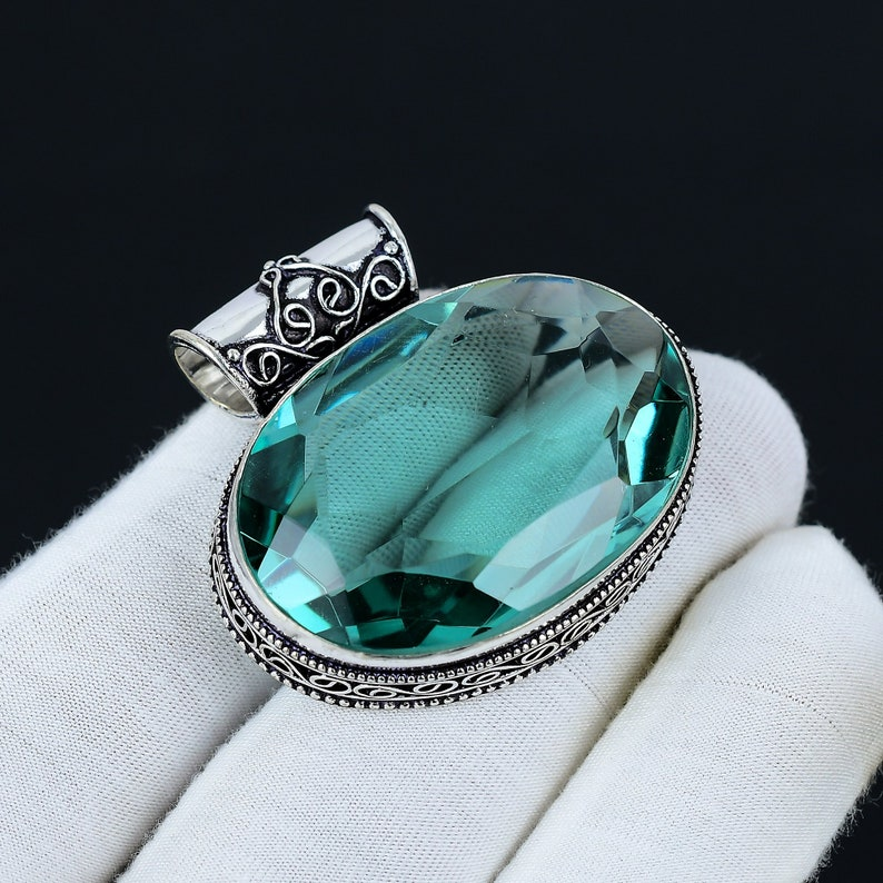 Jewelry pendant with a large green gemstone on a white cushion against a black background