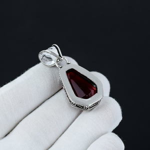 Silver pendant with a red gemstone held by a white gloved hand against a black background