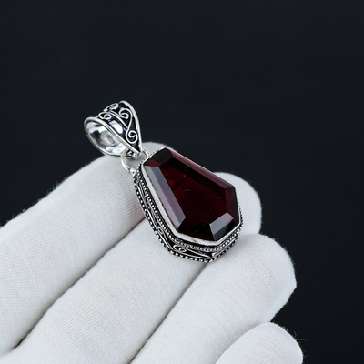 Garnet pendant with silver setting held by a gloved hand against a black background
