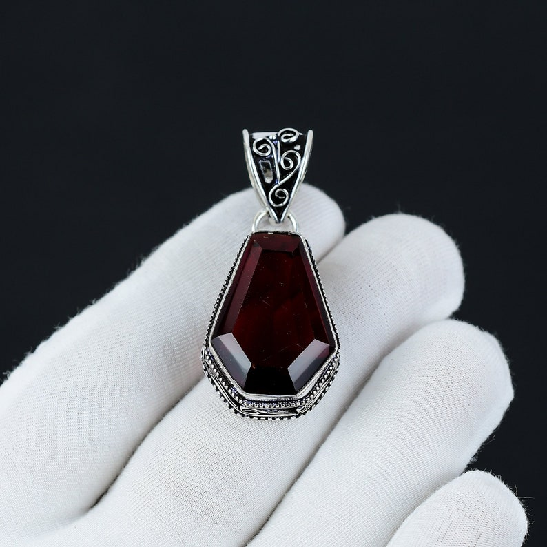 Garnet pendant with silver setting held by a gloved hand against a black background