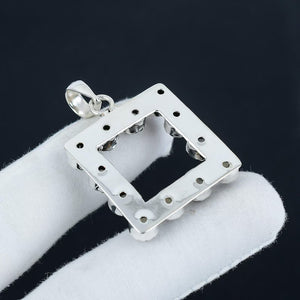 Silver square pendant on a white cushion with a black background