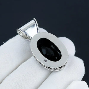 Silver pendant with a black gemstone on a white cloth against a dark background