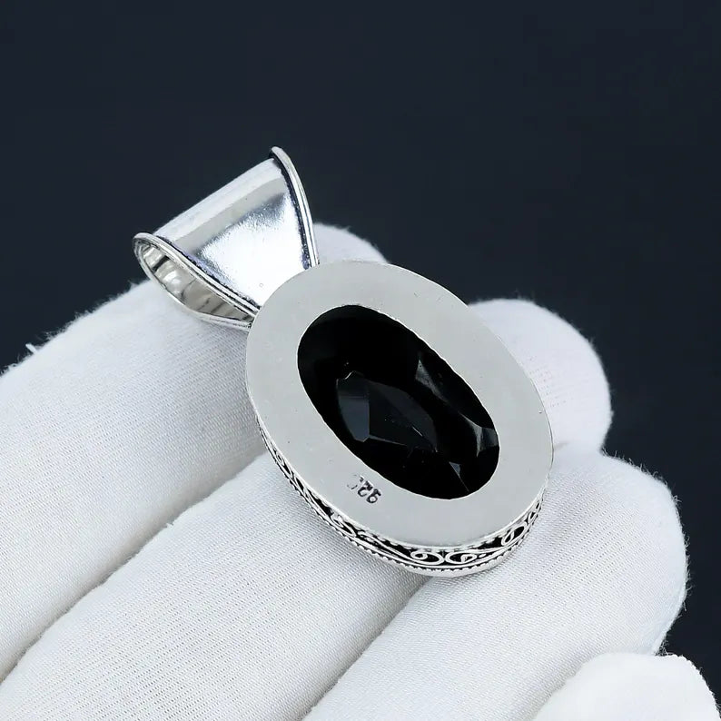 Silver pendant with a black gemstone on a white cloth against a dark background