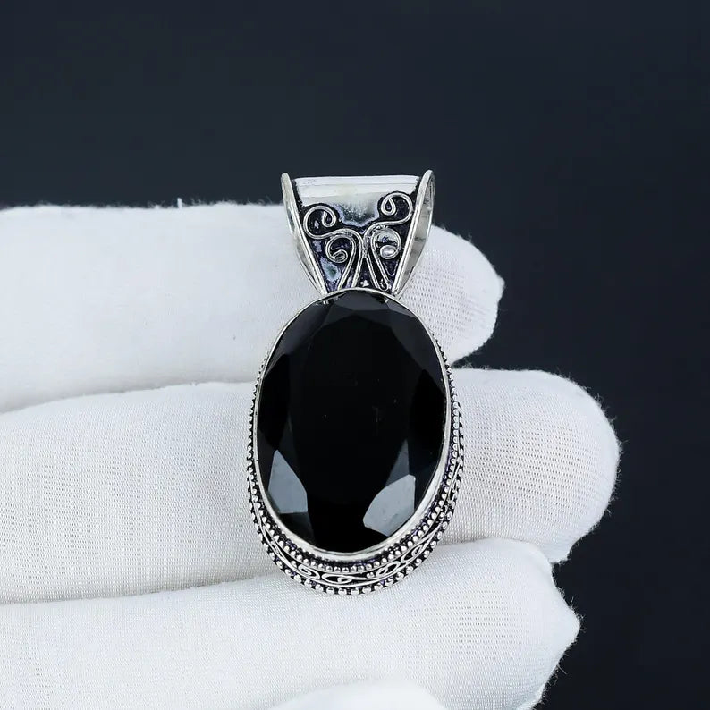Black stone pendant with silver frame held by a white gloved hand against a black background