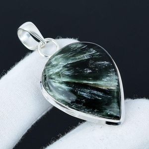 Teardrop-shaped pendant with green crystal on a white cushion against a black background