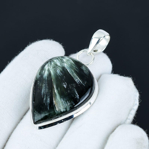 Teardrop-shaped pendant with a black and green stone held by a white gloved hand against a dark background