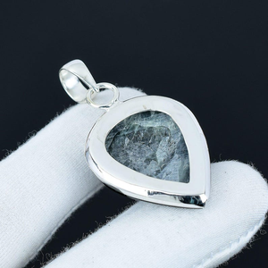 Silver pendant with a heart-shaped stone on a white cushion against a black background