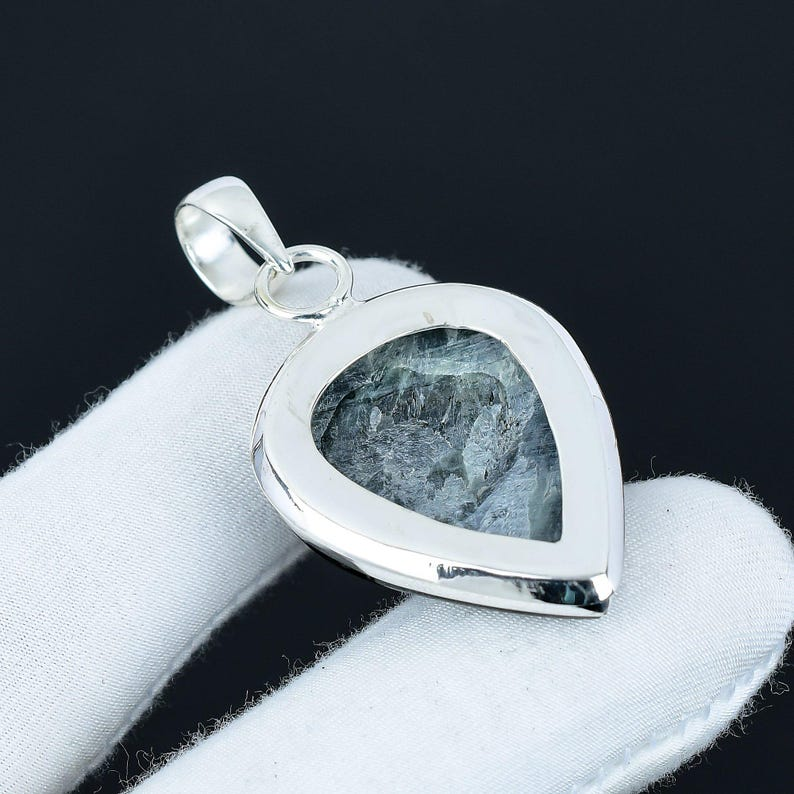 Silver pendant with a heart-shaped stone on a white cushion against a black background