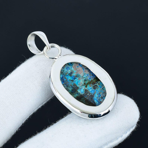 Silver pendant with a blue and green stone on a white cushion against a black background
