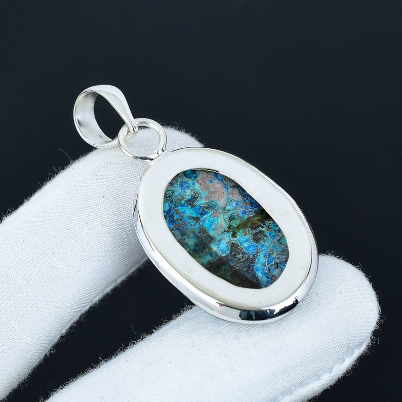 Silver pendant with a blue and green stone on a white cushion against a black background