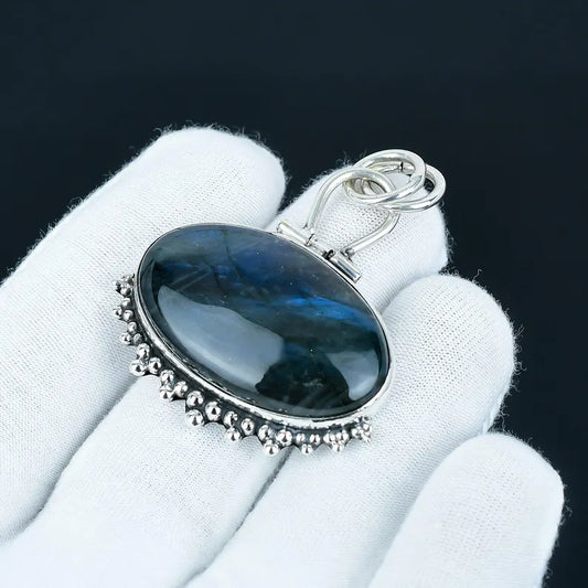 Silver pendant with a dark blue stone held by a gloved hand against a black background