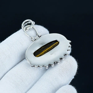 Silver pendant with a central stone held in a white glove against a black background